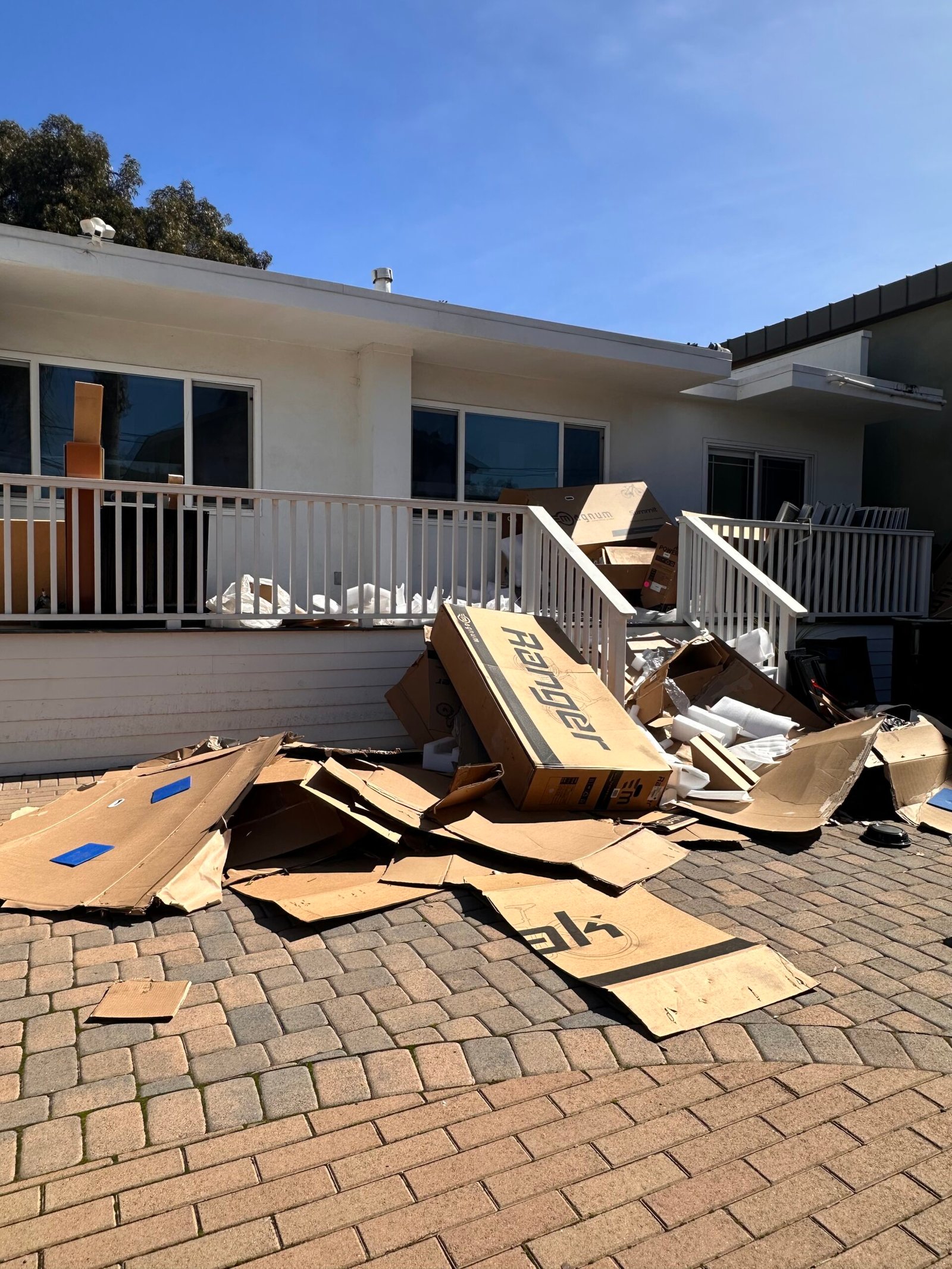 Foreclosure Cleanouts A large pile of flattened cardboard boxes scattered in a driveway/patio in front of the house.